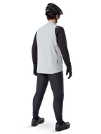 Alpinestars Colete Térmico A-Dura, Cinza Titanium, vista traseira de modelo a usar o colete de ciclismo com isolamento sobre uma camisola de manga comprida preta e calças escuras, com capacete de BTT e luvas pretas, concebido para ciclismo fora de estrada em climas frios