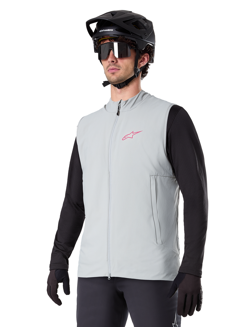 Colete Térmico Alpinestars A-Dura, cinzento Titanium, colete térmico de ciclismo, usado sobre uma camisola preta de manga comprida com capacete de BTT e luvas pretas, com logótipo rosa no peito e bolsos laterais verticais com fecho