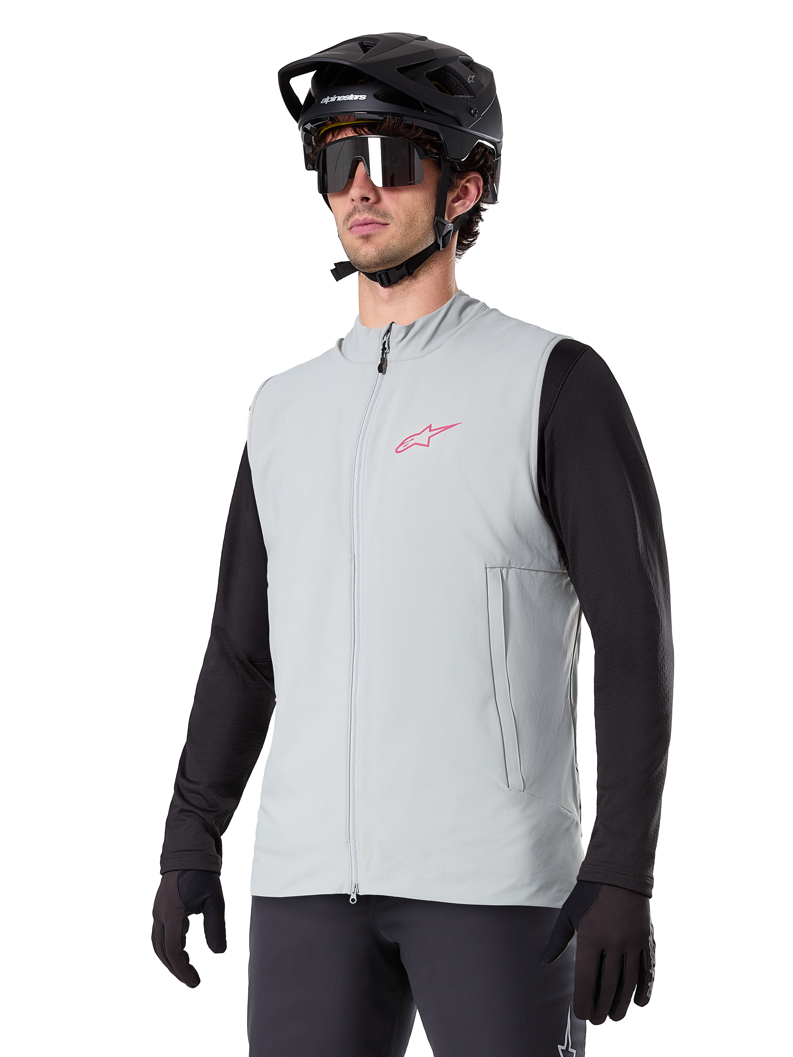 Colete Térmico Alpinestars A-Dura, cinzento Titanium, colete térmico de ciclismo, usado sobre uma camisola preta de manga comprida com capacete de BTT e luvas pretas, com logótipo rosa no peito e bolsos laterais verticais com fecho