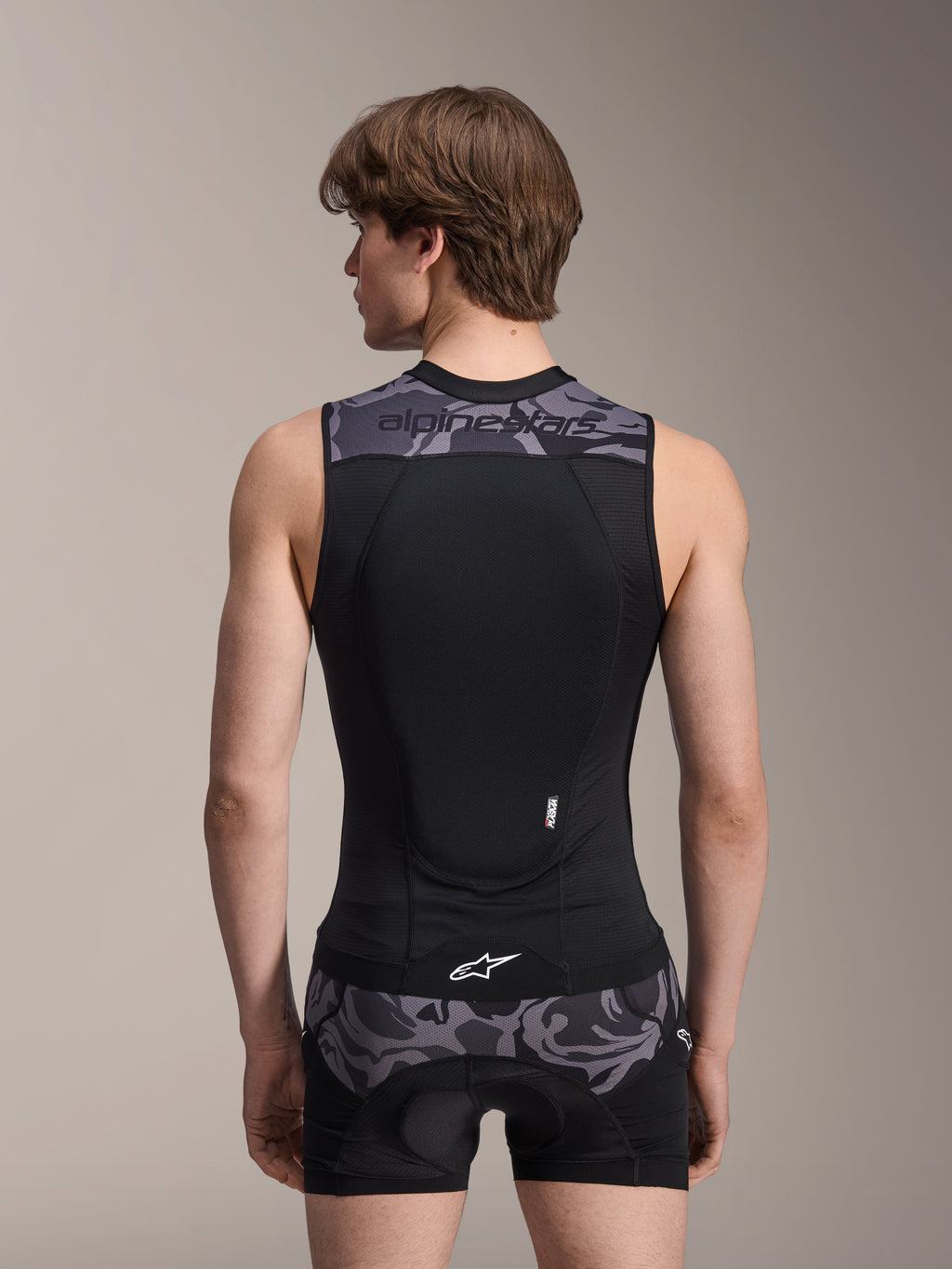 Colete de Proteção Alpinestars A-Motion Plasma, Black Camo, vista traseira num modelo masculino, com construção em malha respirável, protetor de costas Nucleon Plasma integrado, detalhes de camuflagem cinzenta nos ombros e na cintura, e logótipo Alpinestars.