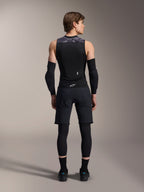 Colete de Proteção Alpinestars A-Motion Plasma, vista posterior, preto com detalhes camuflados cinzentos nos ombros, modelo a usar cotoveleiras pretas, calções de ciclismo sobre leggings e sapatos de ciclismo pretos, destacando o protetor de costas integrado