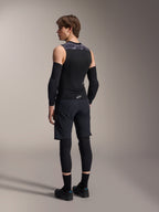 Modelo masculino visto de costas a usar o Colete de Proteção Alpinestars A-Motion Plasma, Black Camo, design em malha sem mangas com protetor de costas integrado, padrão camuflado cinzento nos ombros, usado com protetores de cotovelo pretos e calções de BTT, equipamento de ciclismo profissional.