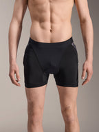 Boxers de Proteção Alpinestars A-Motion Plasma, calções de proteção para BTT, pretos com detalhes em camuflado preto, vista frontal num modelo masculino, com malha elástica respirável e proteção de anca integrada para desempenho no ciclismo.