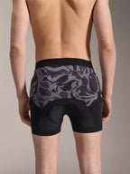 Alpinestars A-Motion Plasma Protection Boxers, calções de proteção para BTT, camuflado preto, vista traseira num modelo, com o logótipo Alpinestars num painel de malha camuflada, almofada de camurça integrada e bolsos para proteção de anca, camada de base respirável para ciclismo fora de estrada