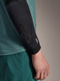 Alpinestars A-Motion Plasma Elbow Sleeve, cotoveleira de proteção para MTB, preta, vista de pormenor no braço com camisola verde-azulado, com logótipo tonal Astars e marca Nucleon Plasma, design em malha de perfil fino para ciclismo todo-o-terreno