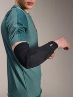Cotoveleira Alpinestars A-Motion Plasma, protetor de cotovelo para ciclismo, preta, usada por um ciclista com uma camisola verde-azulado, com o logótipo Alpinestars e a marca Nucleon Plasma, design elegante e respirável para proteção de BTT