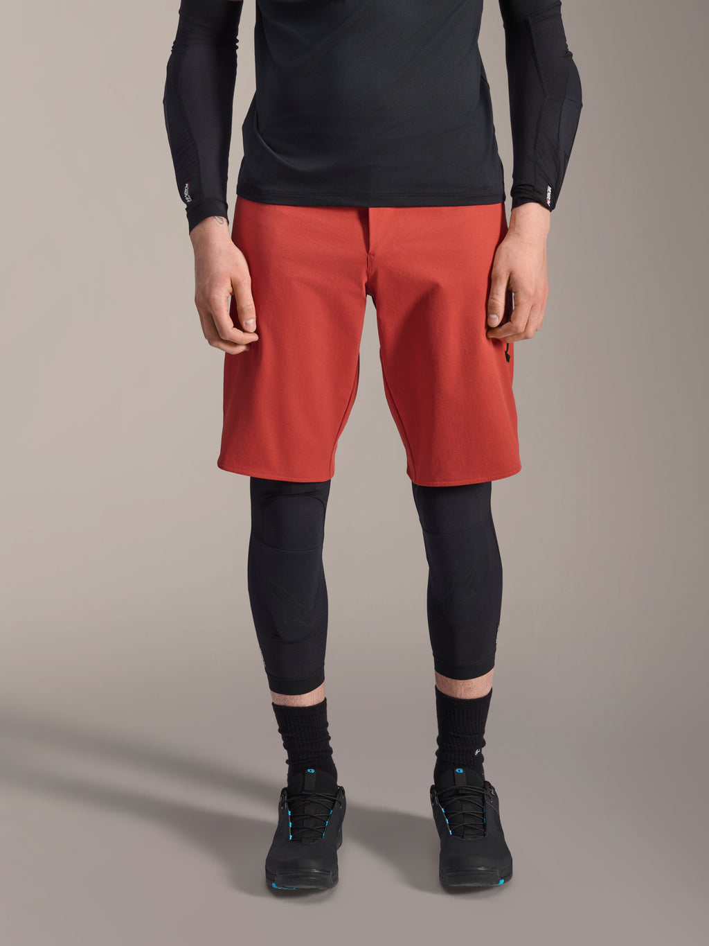 Alpinestars A-Motion Plasma Knee Sleeve, joelheira de proteção para MTB preta, usada com calções vermelhos e camisola de manga comprida preta, design ergonómico de perfil fino, construção em malha leve para condução off-road