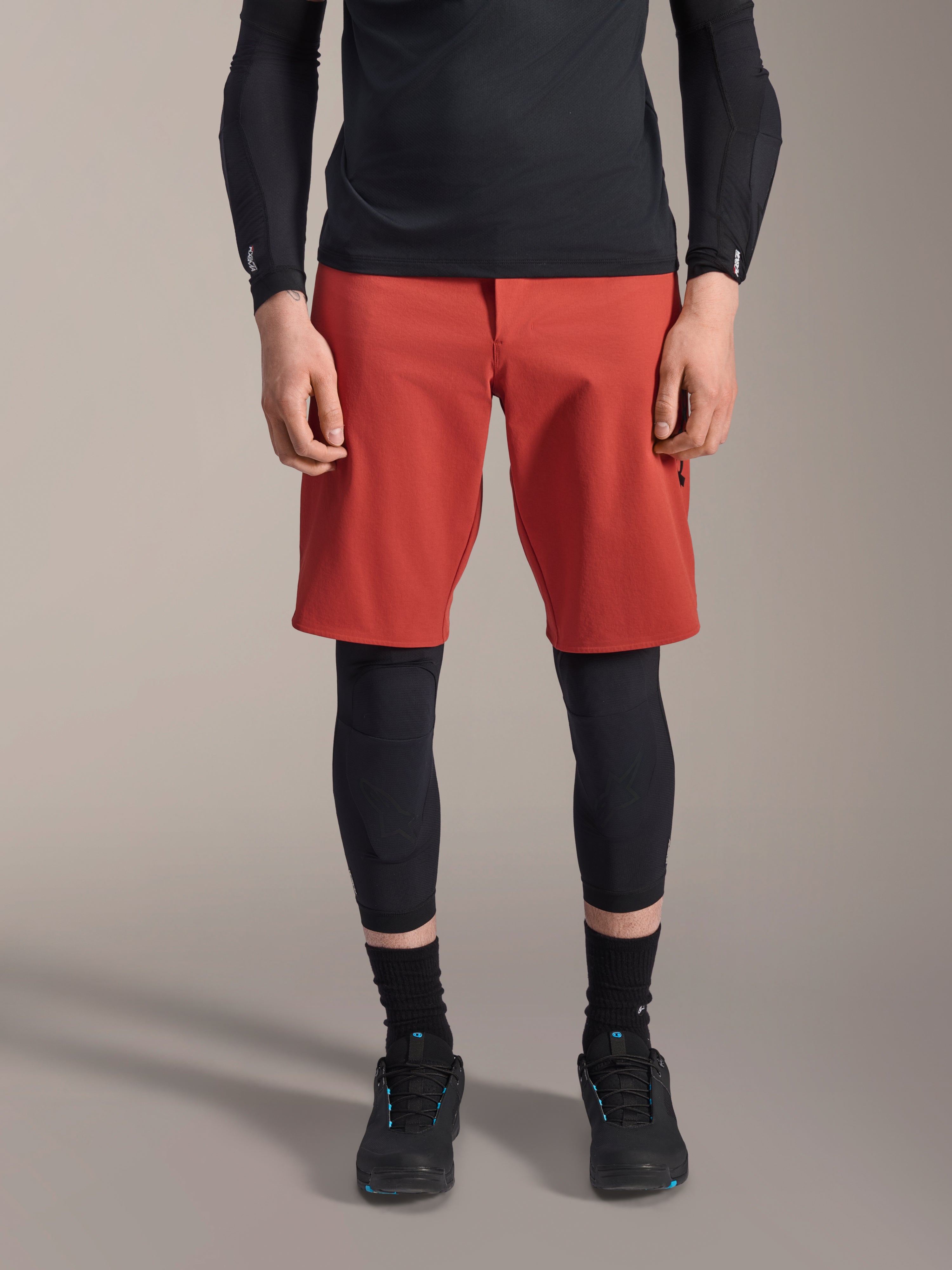 Alpinestars A-Motion Plasma Knee Sleeve, joelheira de proteção para MTB preta, usada com calções vermelhos e camisola de manga comprida preta, design ergonómico de perfil fino, construção em malha leve para condução off-road