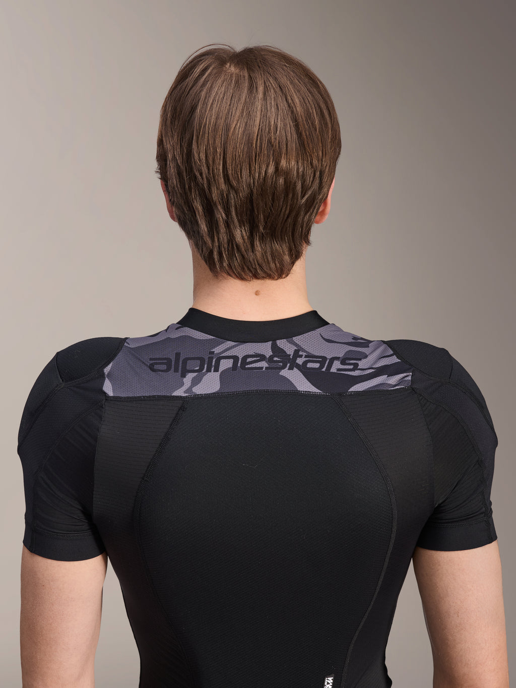 Casaco de Proteção Alpinestars A-Motion Plasma - Manga Curta, vista traseira do tronco superior, preto com painel camuflado cinzento nos ombros com logótipo Alpinestars, construção em malha elástica respirável para proteção de BTT