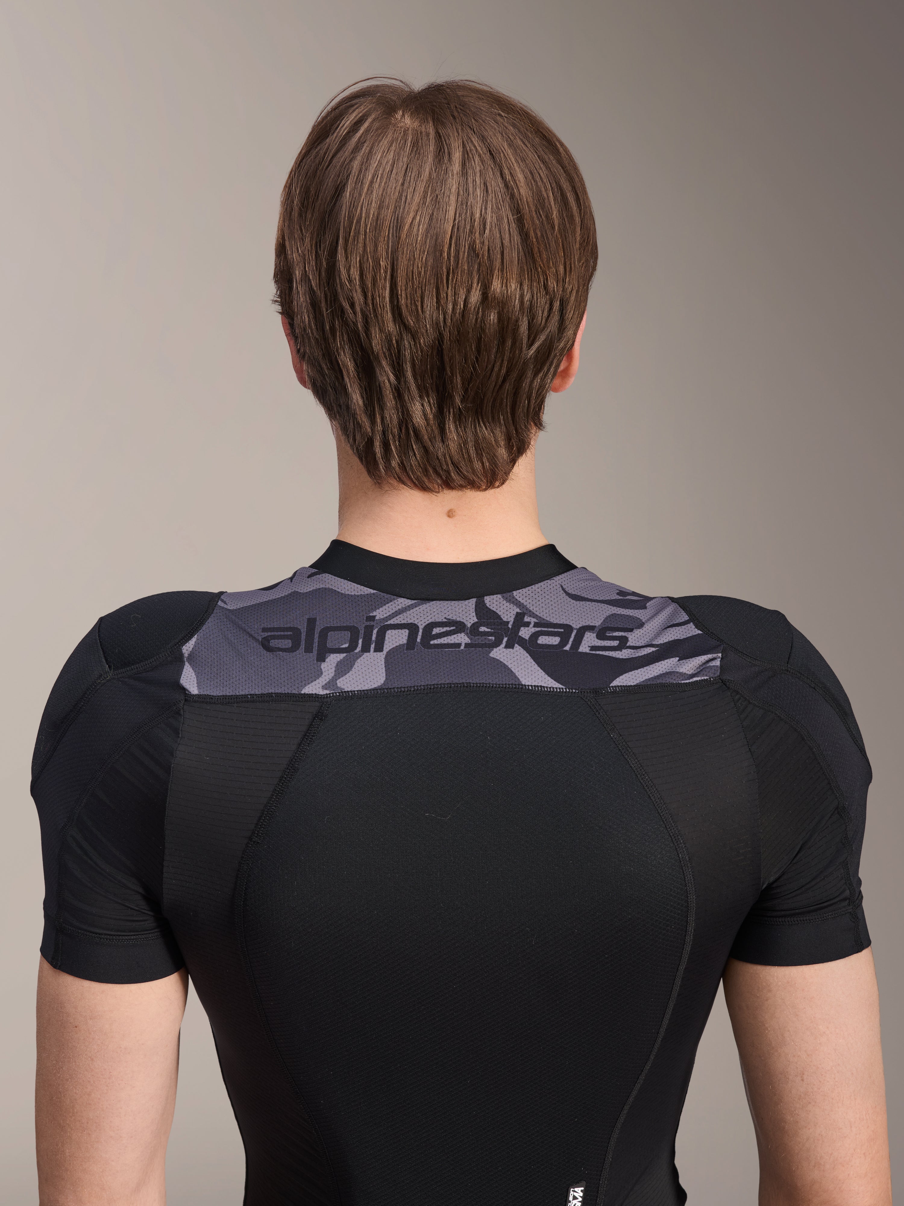 Casaco de Proteção Alpinestars A-Motion Plasma - Manga Curta, vista traseira do tronco superior, preto com painel camuflado cinzento nos ombros com logótipo Alpinestars, construção em malha elástica respirável para proteção de BTT