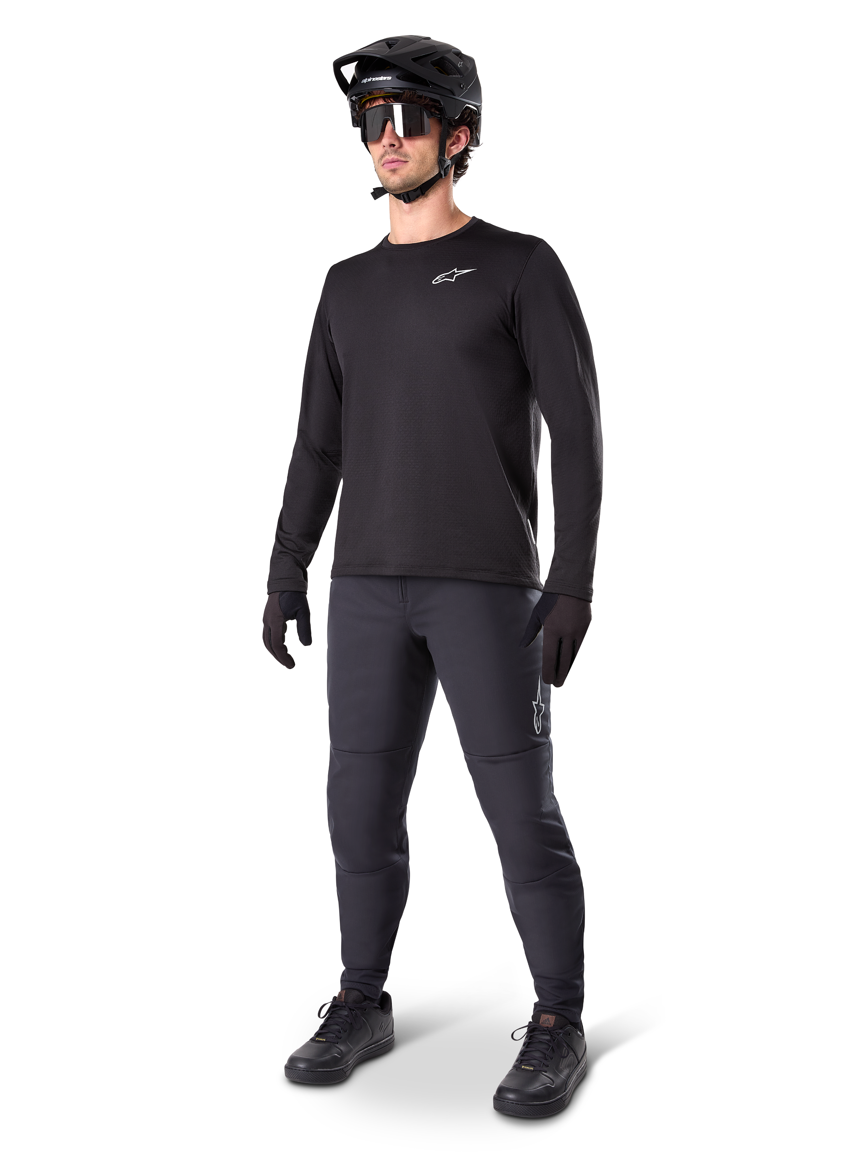 Mountain bike rider wearing Alpinestars A-Dura Thermal Pants, Black, styled with a black long-sleeve jersey, black helmet, and sunglasses, featuring a silver Alpinestars logo on the left thigh, designed for cold-weather trail riding