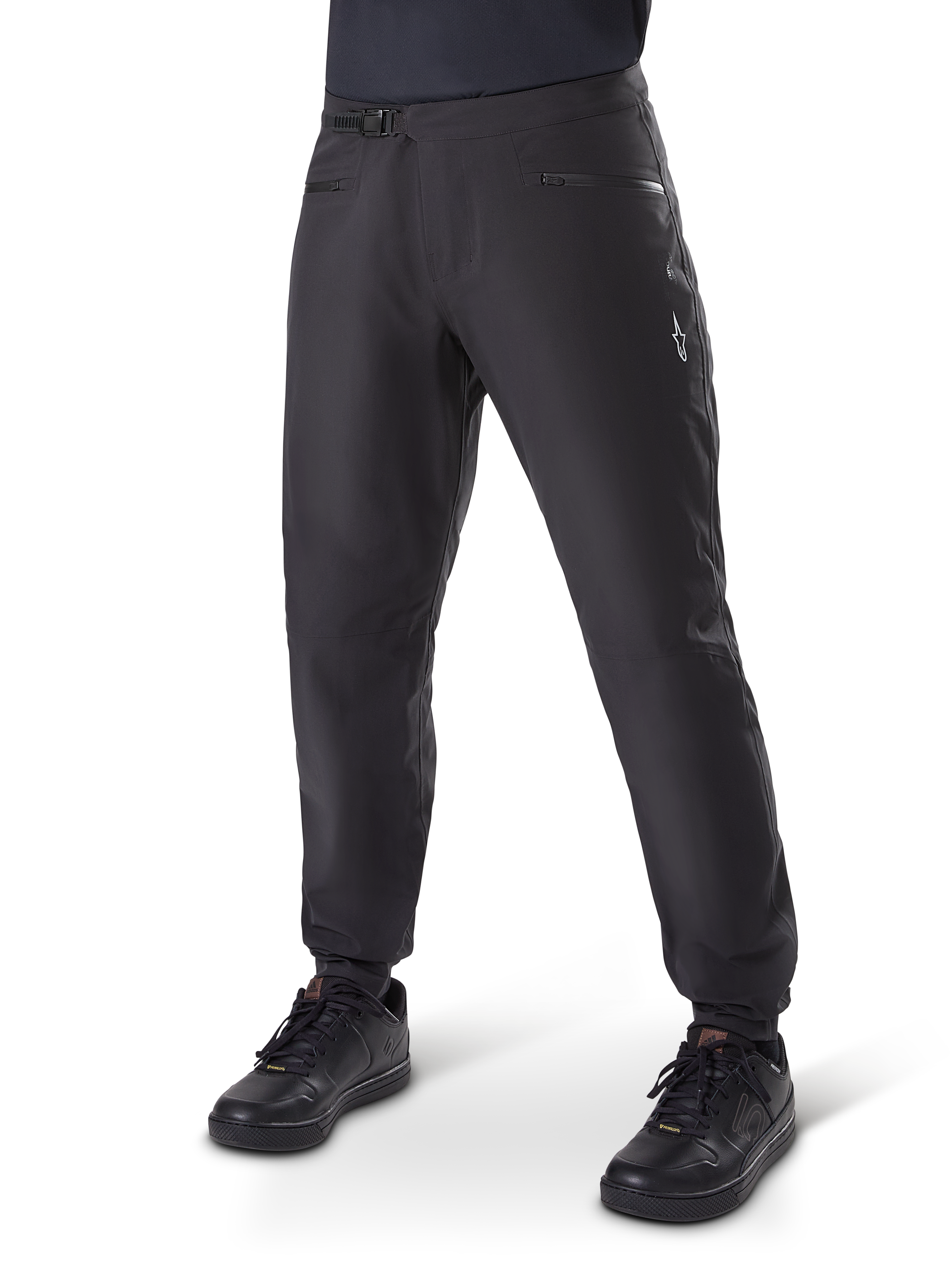 Alpinestars A-Dura Waterproof Pants, MTB Cycling Pants, Black, featuring a ratchet waist closure, zippered pockets, and a white Astars logo on the thigh, shown worn with black cycling shoes for all-weather trail riding