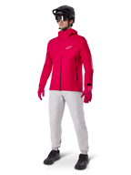 Modelo a usar Calças Impermeáveis Alpinestars A-Dura em cinzento Titanium, combinadas com um casaco impermeável vermelho vivo e luvas a condizer, capacete de BTT preto com óculos e sapatos pretos, equipamento completo de BTT para trilhos molhados