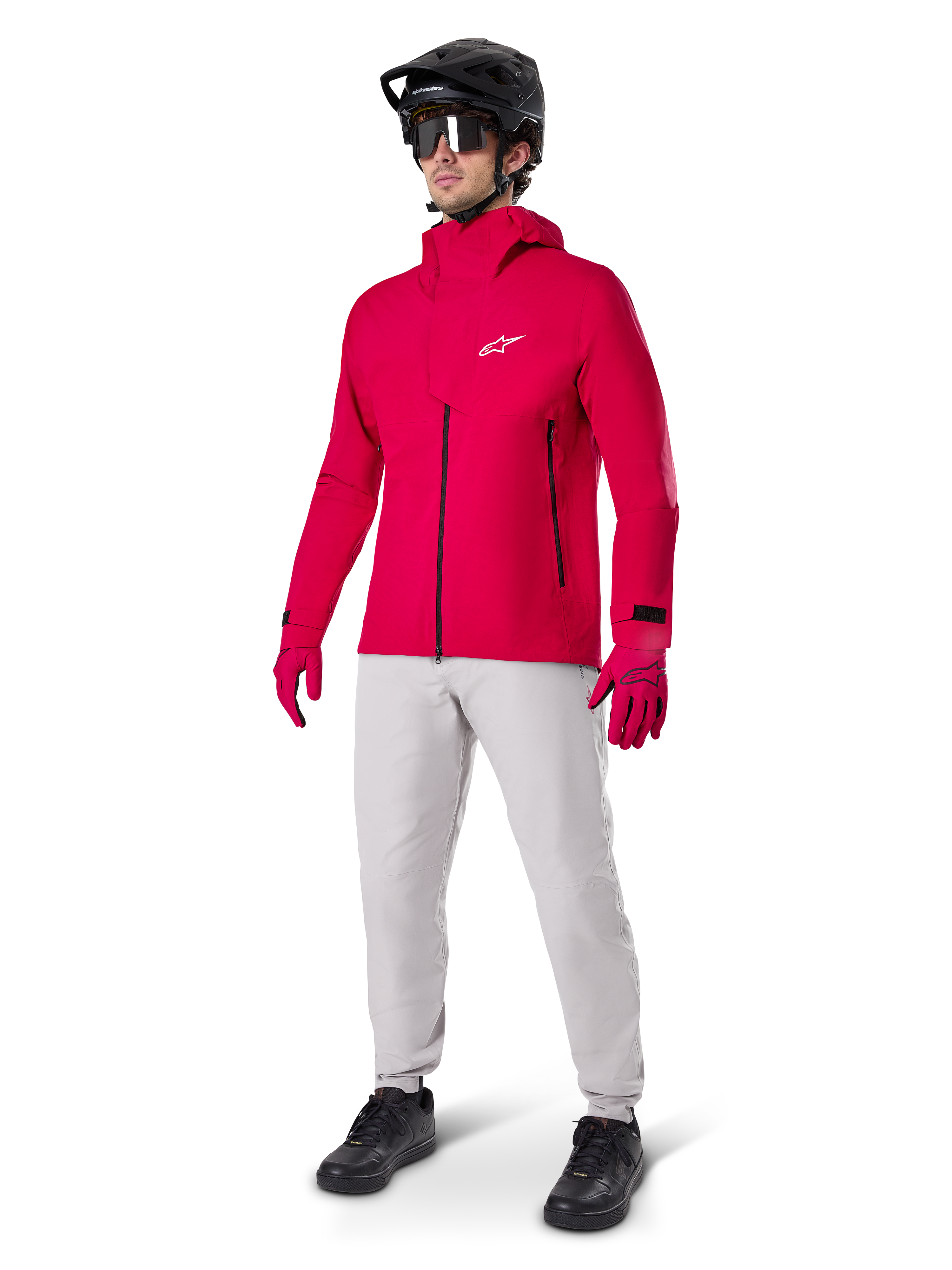 Modelo a usar Calças Impermeáveis Alpinestars A-Dura em cinzento Titanium, combinadas com um casaco impermeável vermelho vivo e luvas a condizer, capacete de BTT preto com óculos e sapatos pretos, equipamento completo de BTT para trilhos molhados
