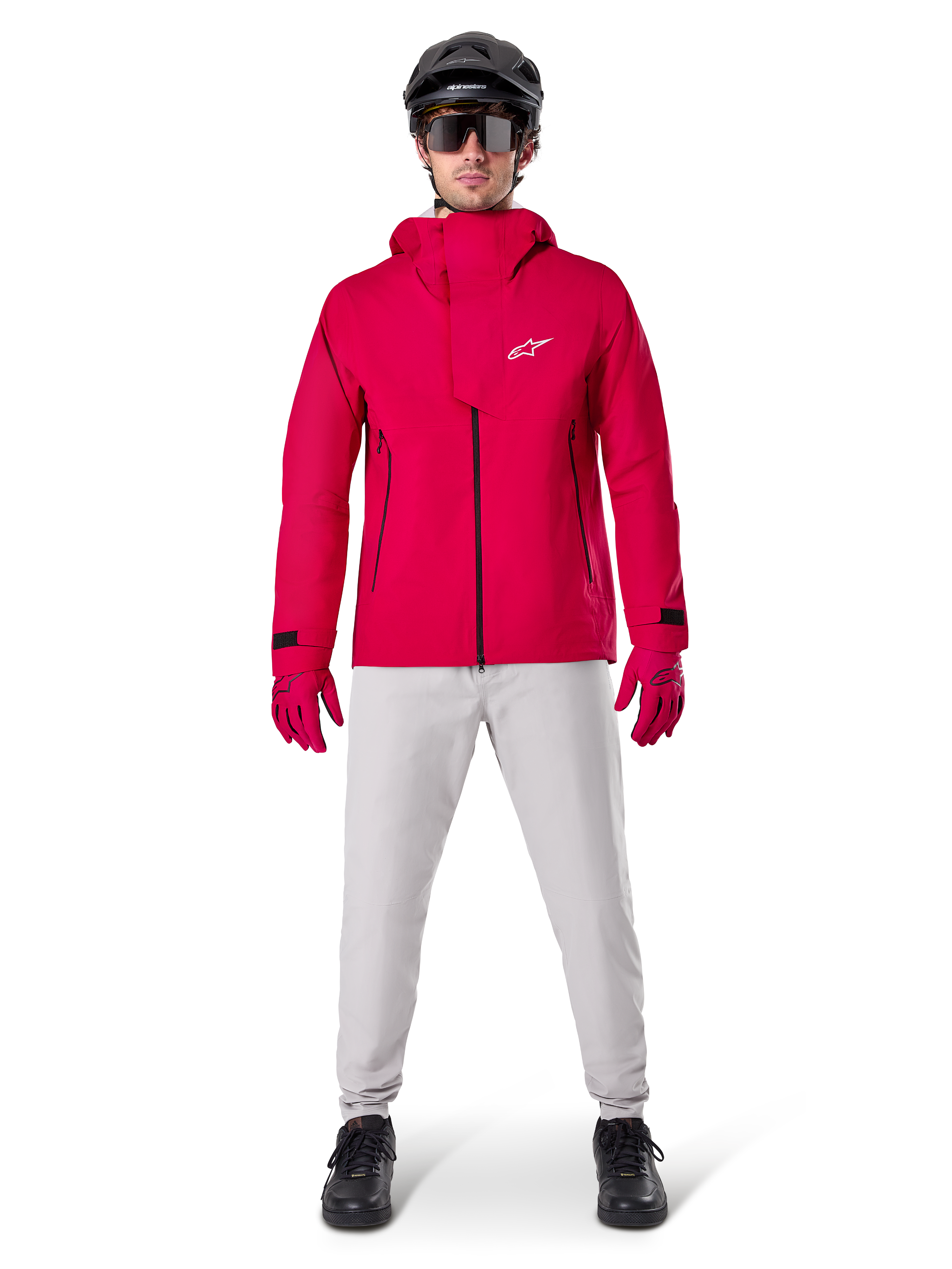 Calças Impermeáveis Alpinestars A-Dura, calças de BTT, cinzento Titanium, usadas com um casaco vermelho vivo com capuz, luvas vermelhas e um capacete de BTT preto, equipamento de ciclismo profissional impermeável para condições de trilhos molhados