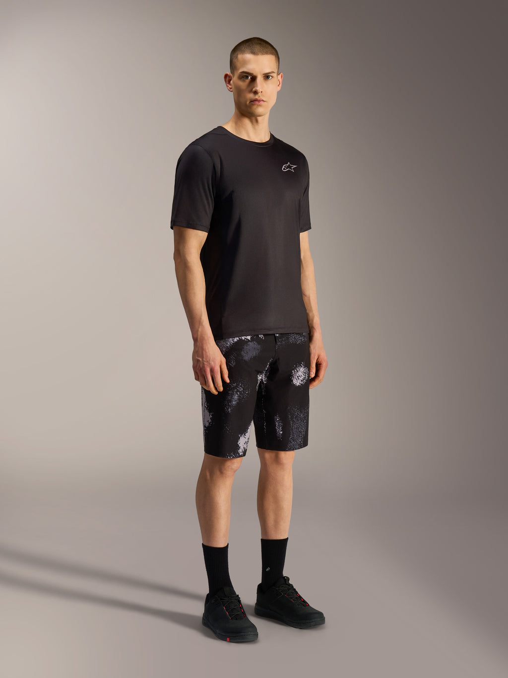Calções A-Dura Ride Alpinestars em Black Camo, com padrão camuflado cinzento, t-shirt e calçado pretos.