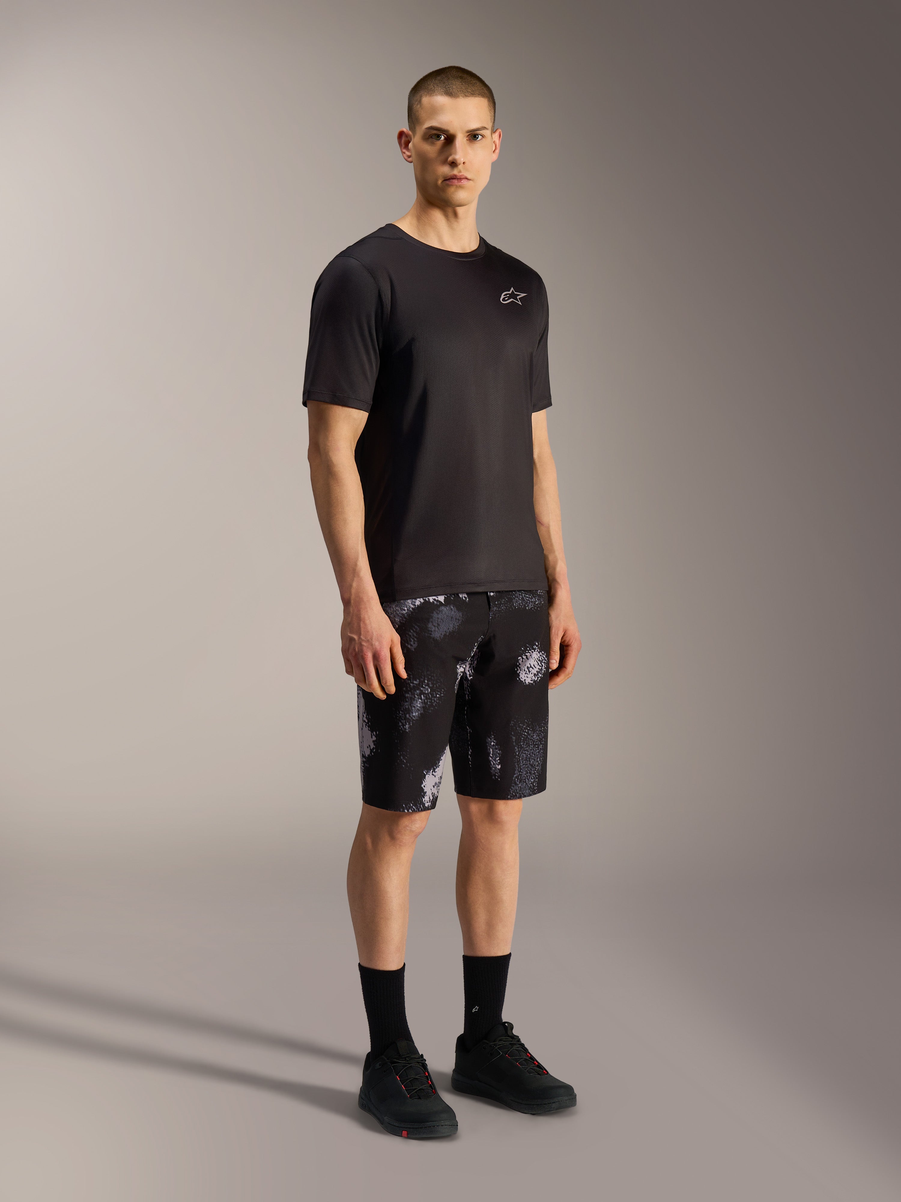 Calções A-Dura Ride Alpinestars em Black Camo, com padrão camuflado cinzento, t-shirt e calçado pretos.