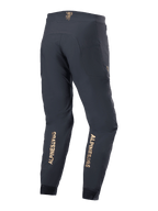 Calças Alpinestars A-Aria Elite, calças de BTT, pretas, vista traseira com logótipos verticais dourados na parte inferior das pernas, ajuste de desempenho com cós absorvente e bolsos com fecho, concebidas para ciclismo de montanha