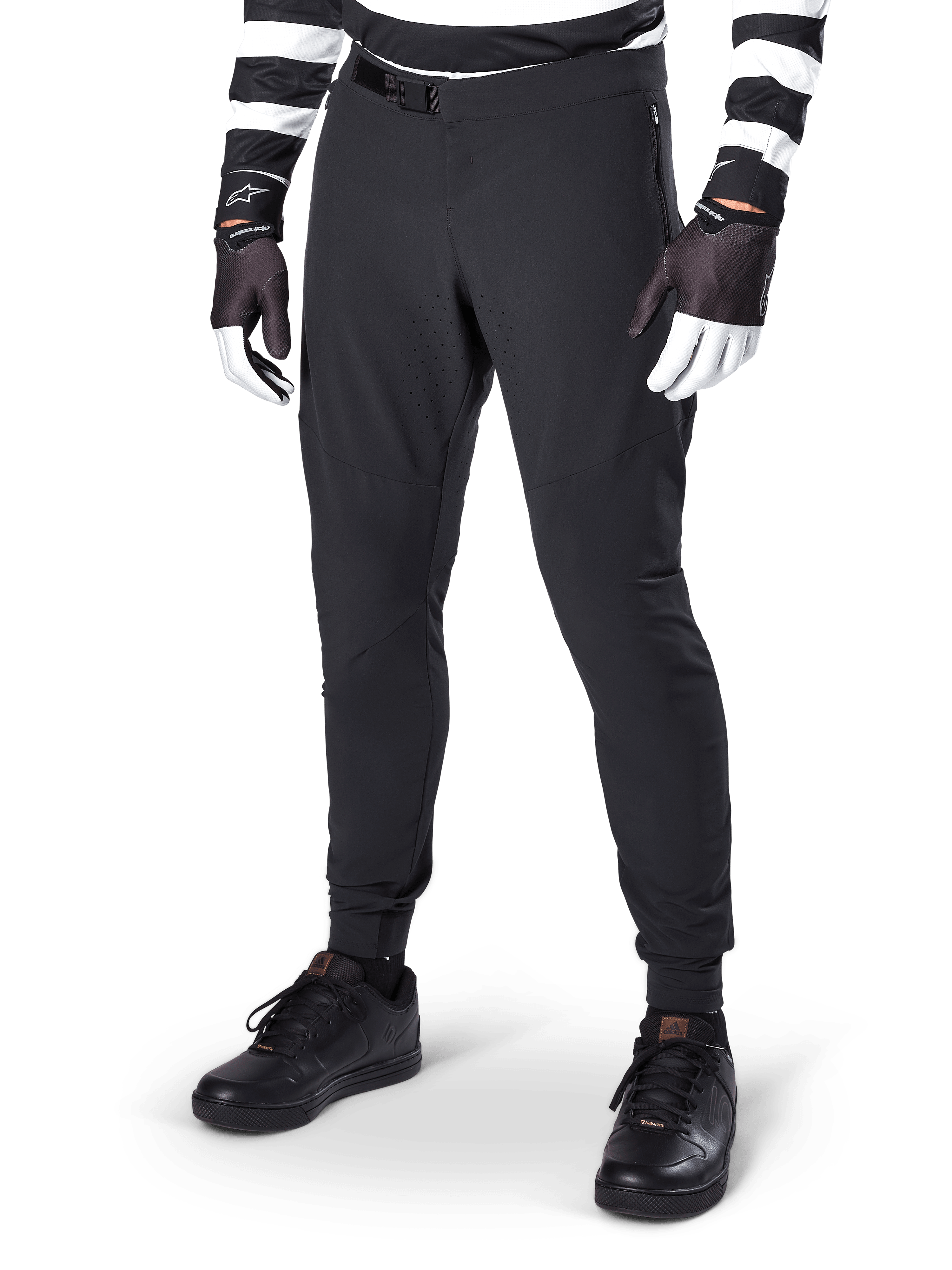 Alpinestars A-Aria Elite Pants, calças pretas de BTT, com ventilação cortada a laser nas coxas e fecho de fivela magnética, usadas com camisola e luvas às riscas pretas e brancas, equipamento de BTT de performance para ciclismo todo-o-terreno