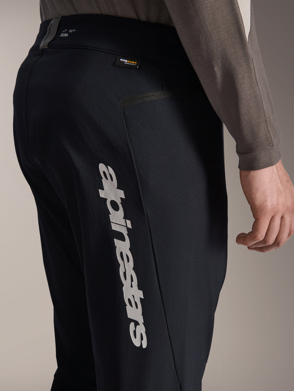 Calças Alpinestars A-Dura Elite, calças de BTT pretas, vista lateral com um grande logótipo vertical Alpinestars na perna, etiqueta de tecido Cordura e bolso lateral com fecho, vestuário técnico de ciclismo para off-road
