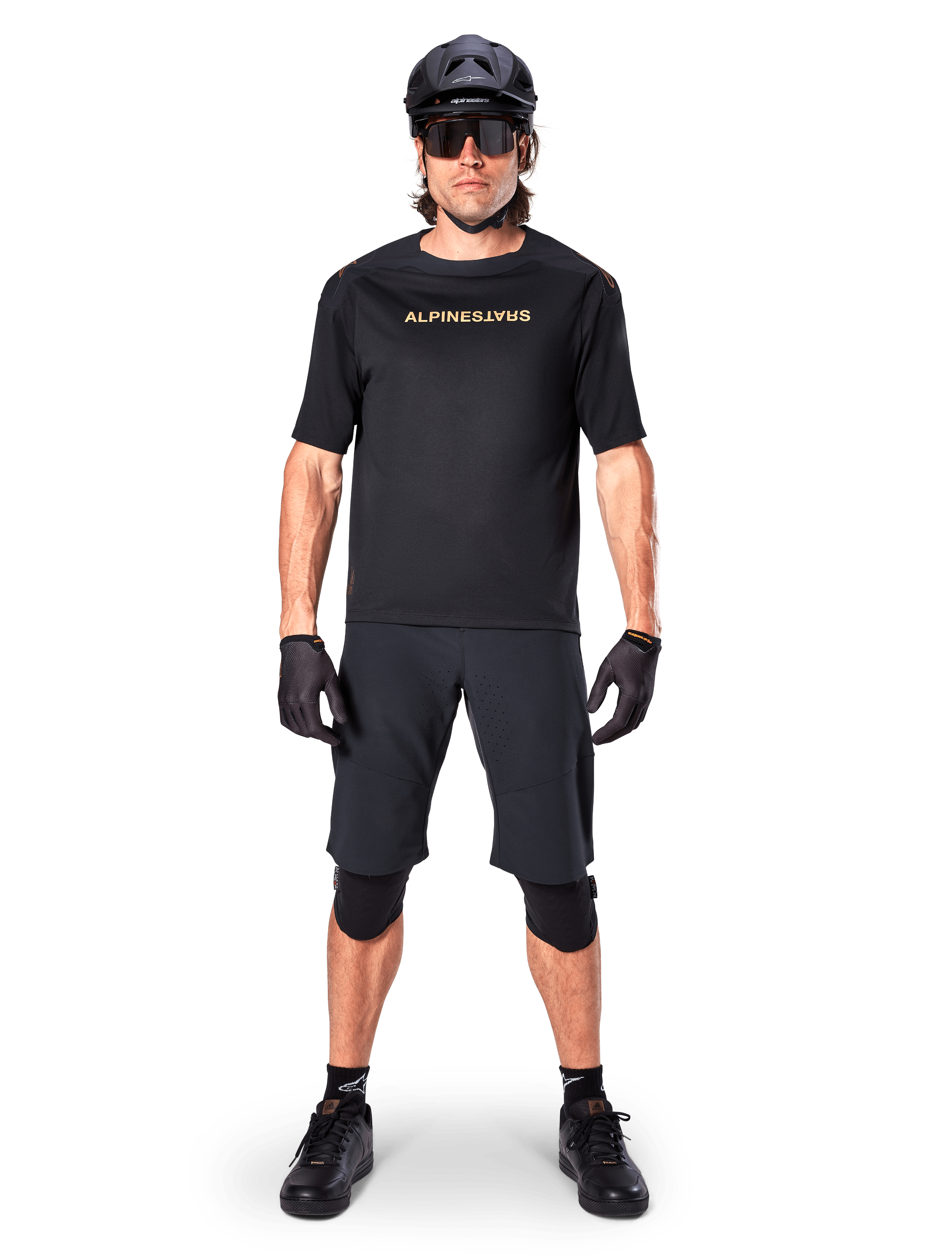 Ciclista de BTT masculino a usar os calções Alpinestars A-Aria Elite em preto, combinados com uma camisola de manga curta Alpinestars preta a condizer, capacete, luvas e joelheiras pretas, conjunto completo de equipamento de ciclismo off-road