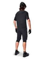 Vista traseira de um ciclista de montanha a usar calções Alpinestars A-Aria Elite em preto, combinados com uma camisola de manga curta preta a condizer, capacete preto, luvas e sapatos de BTT, mostrando um equipamento de performance completo para ciclismo fora de estrada.