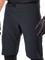 Calções Alpinestars A-Aria Elite em preto, vista detalhada da zona da cintura e das coxas, com fecho de fivela magnética, bolsos com fecho de correr e perfurações de ventilação cortadas a laser, usados com luvas de ciclismo pretas para BTT.