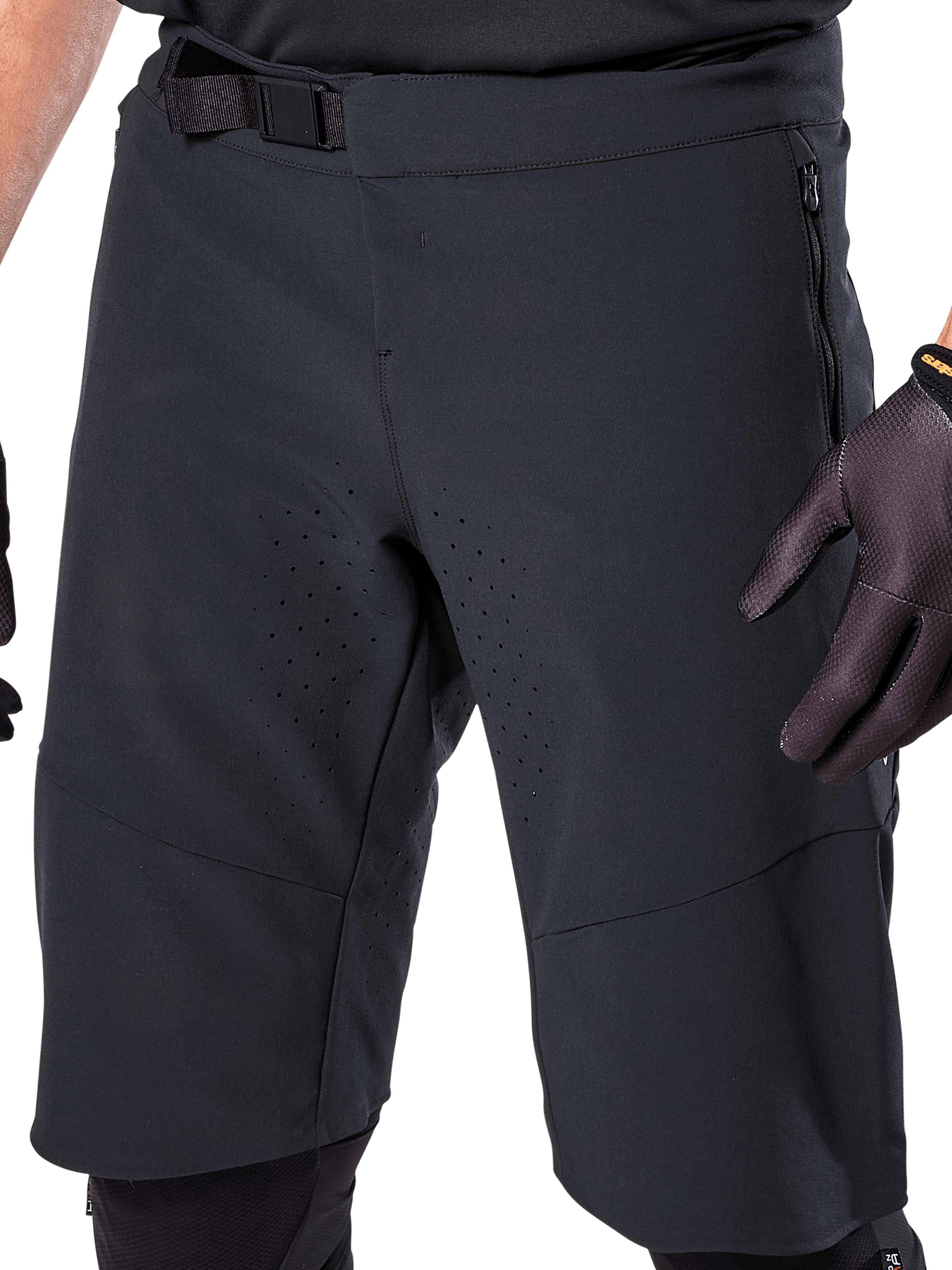 Calções Alpinestars A-Aria Elite em preto, vista detalhada da zona da cintura e das coxas, com fecho de fivela magnética, bolsos com fecho de correr e perfurações de ventilação cortadas a laser, usados com luvas de ciclismo pretas para BTT.
