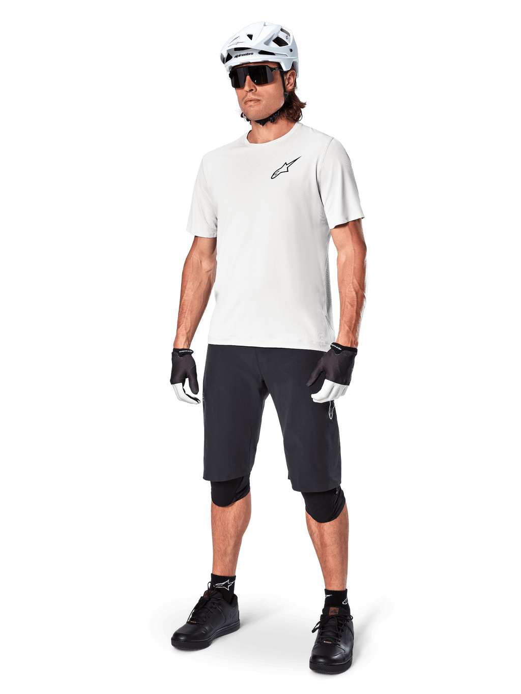Ciclista de montanha masculino a usar calções Alpinestars A-Aria, calções de ciclismo pretos, combinados com uma camisola de manga curta branca, capacete de BTT branco e equipamento de performance preto, conjunto completo para trilhos de todo-o-terreno