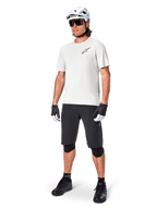 Ciclista de montanha masculino a usar calções Alpinestars A-Aria, calções de ciclismo pretos, combinados com uma camisola de manga curta branca, capacete de BTT branco e equipamento de performance preto, conjunto completo para trilhos de todo-o-terreno