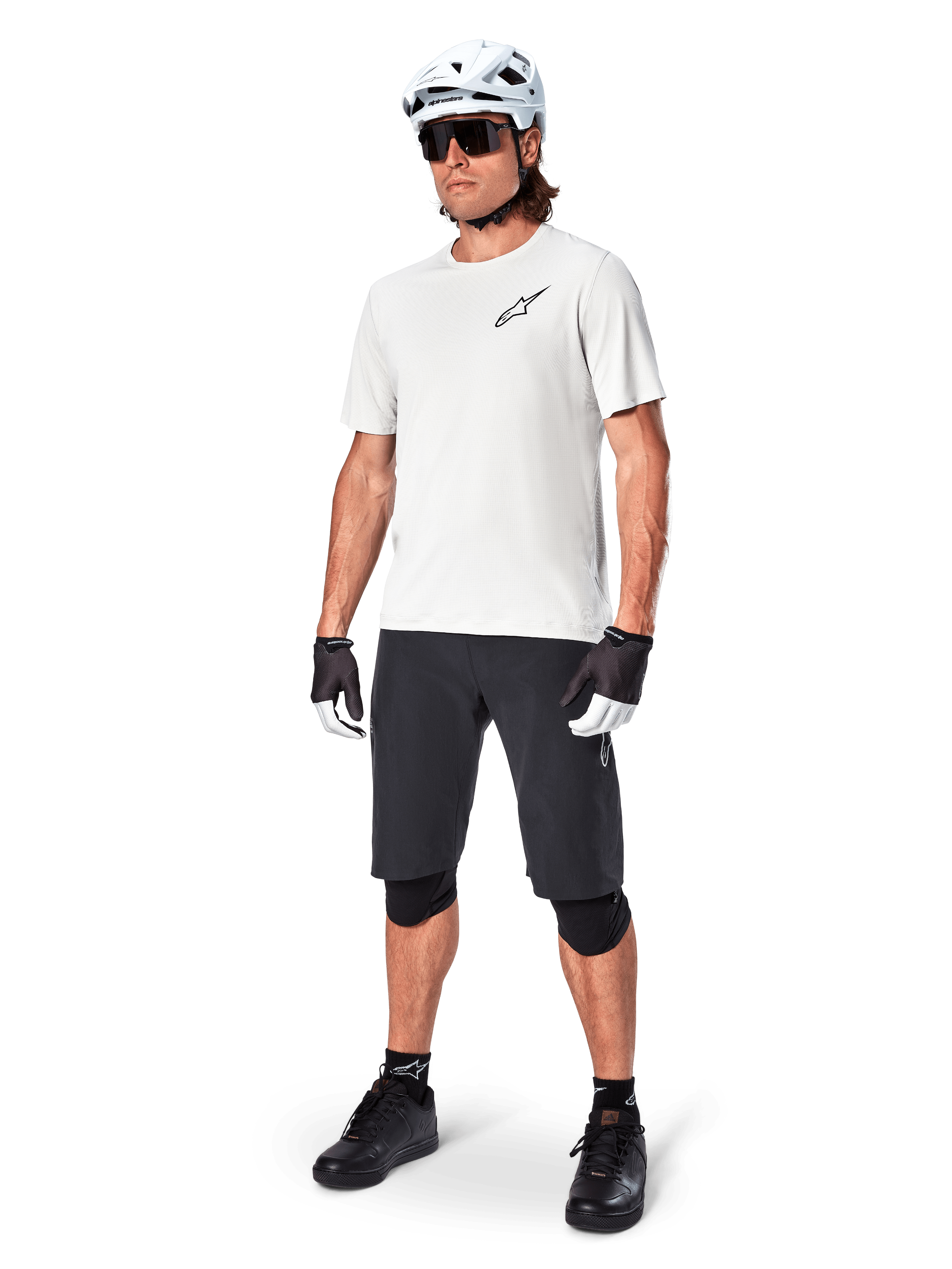 Ciclista de montanha masculino a usar calções Alpinestars A-Aria, calções de ciclismo pretos, combinados com uma camisola de manga curta branca, capacete de BTT branco e equipamento de performance preto, conjunto completo para trilhos de todo-o-terreno
