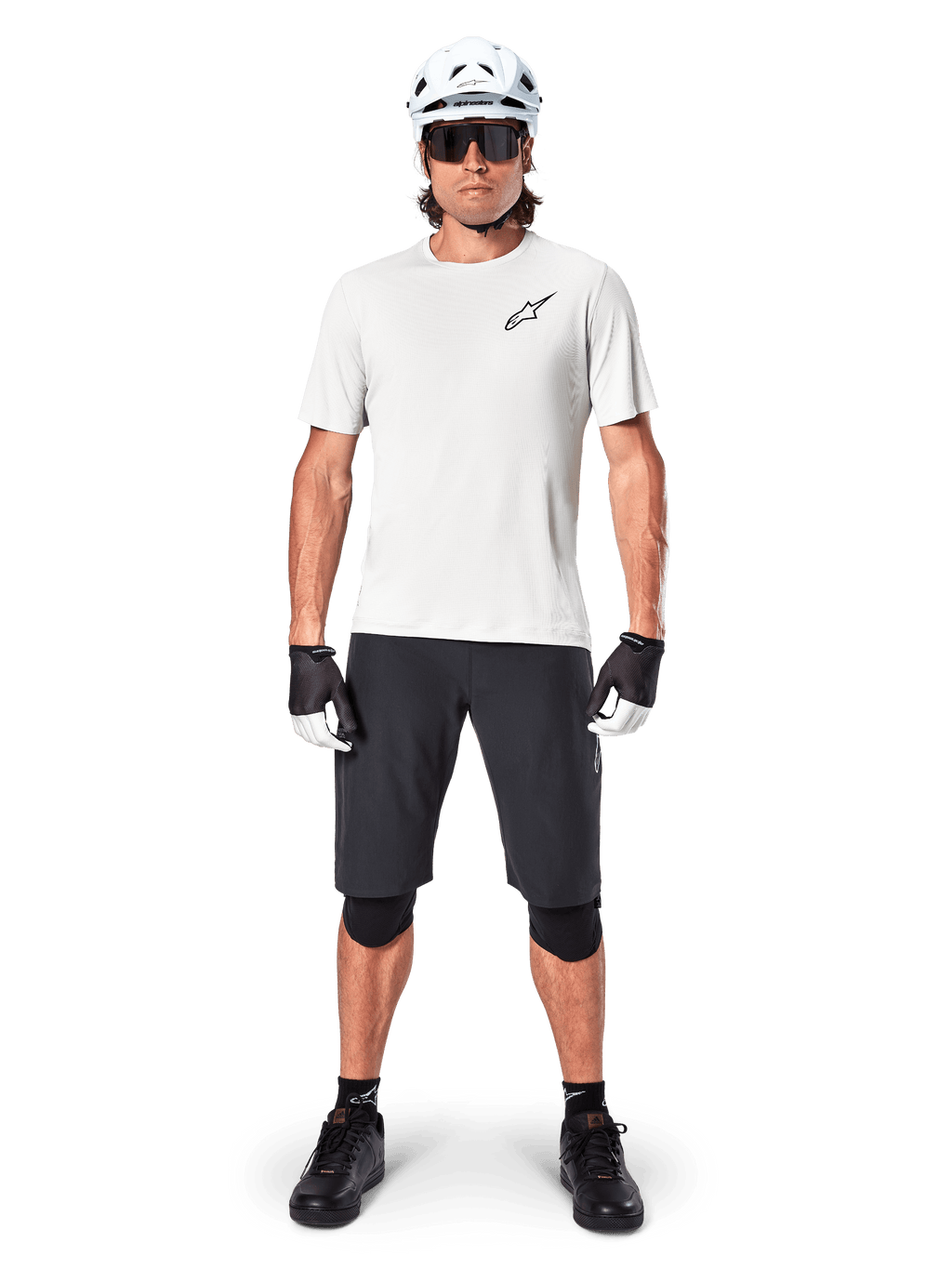Ciclista de montanha masculino a usar calções Alpinestars A-Aria pretos, combinados com uma camisola de performance branca, capacete branco e joelheiras pretas, equipamento profissional de ciclismo fora de estrada numa vista frontal de corpo inteiro