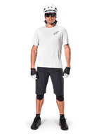 Ciclista de montanha masculino a usar calções Alpinestars A-Aria pretos, combinados com uma camisola de performance branca, capacete branco e joelheiras pretas, equipamento profissional de ciclismo fora de estrada numa vista frontal de corpo inteiro