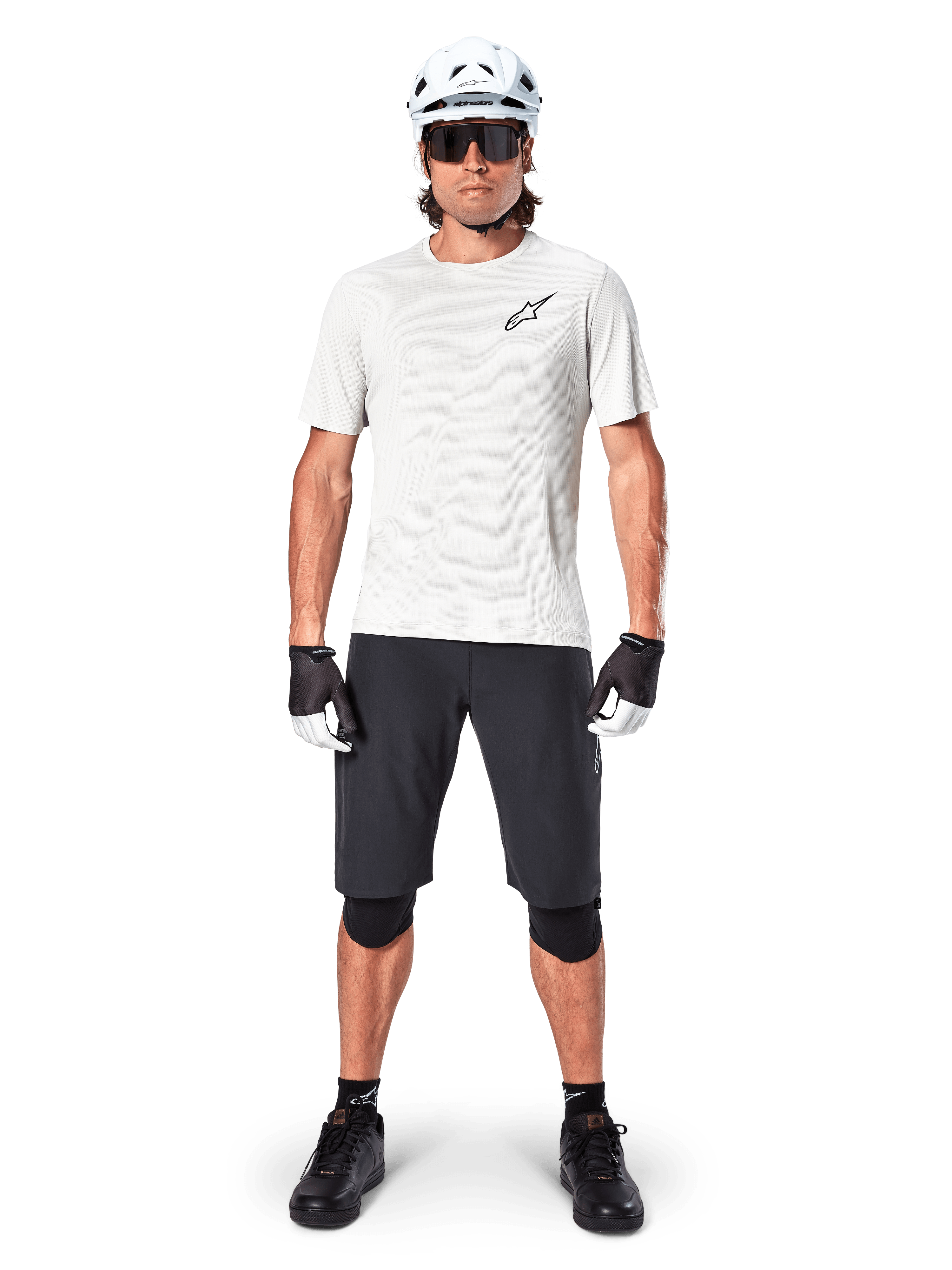 Ciclista de montanha masculino a usar calções Alpinestars A-Aria pretos, combinados com uma camisola de performance branca, capacete branco e joelheiras pretas, equipamento profissional de ciclismo fora de estrada numa vista frontal de corpo inteiro