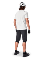 Ciclista de montanha visto de trás a usar calções Alpinestars A-Aria pretos, camisola de performance branca de manga curta, capacete branco, luvas pretas e sapatos de BTT pretos, equipamento de ciclismo para trilhos