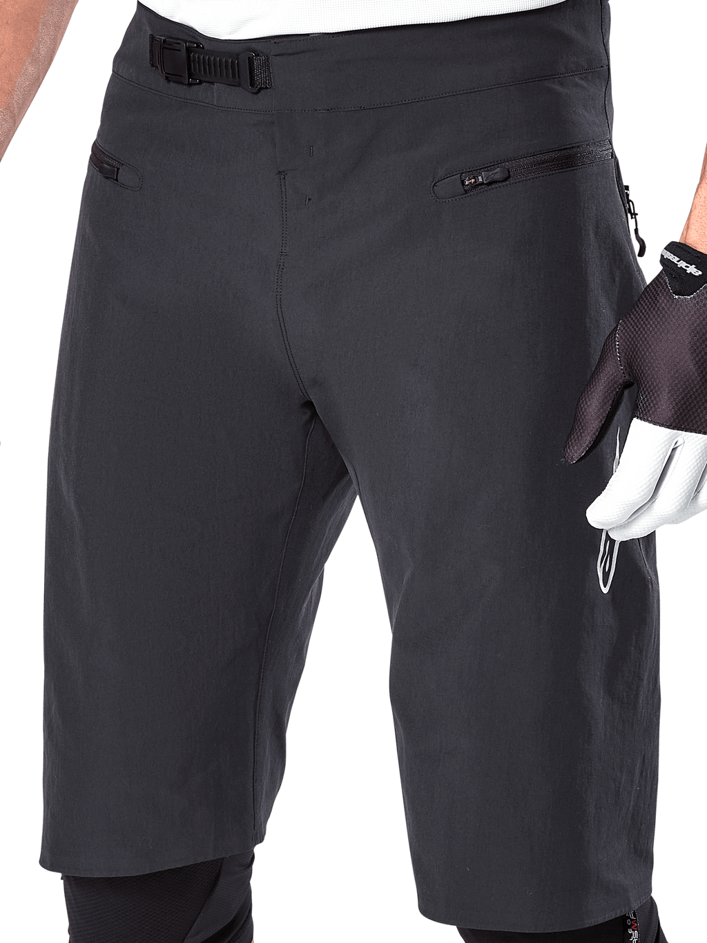 Calções Alpinestars A-Aria, calções de BTT, pretos, pormenor da cintura frontal e das coxas mostrando o sistema de fecho de catraca e bolsos com fecho de correr, usados com luvas de ciclismo pretas e brancas, equipamento de trail de alta performance