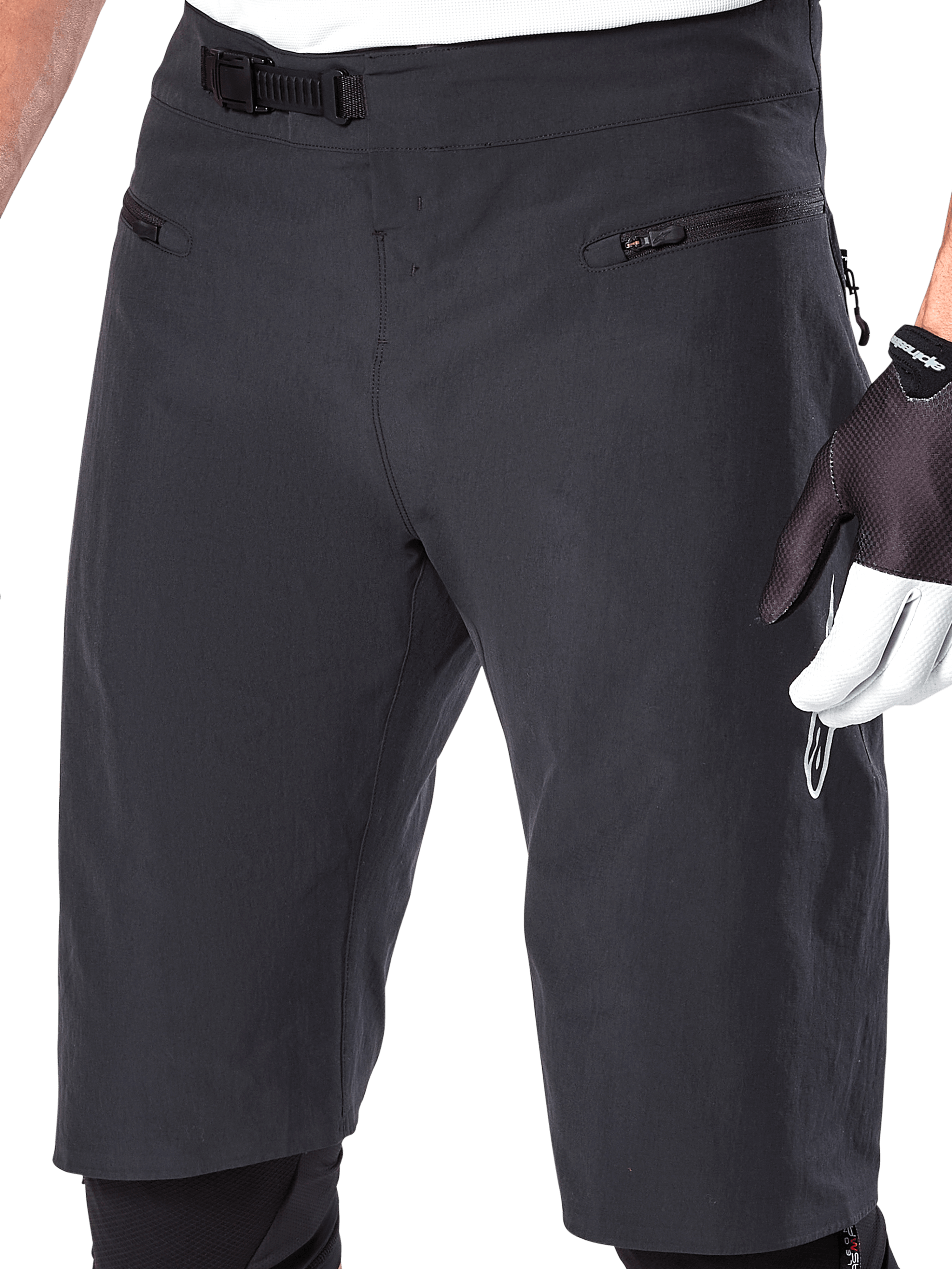 Calções Alpinestars A-Aria, calções de BTT, pretos, pormenor da cintura frontal e das coxas mostrando o sistema de fecho de catraca e bolsos com fecho de correr, usados com luvas de ciclismo pretas e brancas, equipamento de trail de alta performance