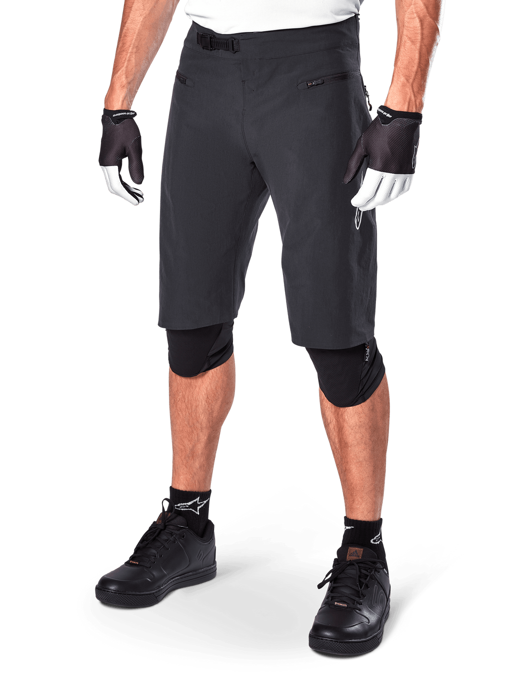 Alpinestars A-Aria Shorts, calções de BTT, pretos, pelo joelho com bolsos frontais com fecho e fivela de catraca ajustável na cintura, usados com joelheiras pretas, meias e luvas de ciclismo
