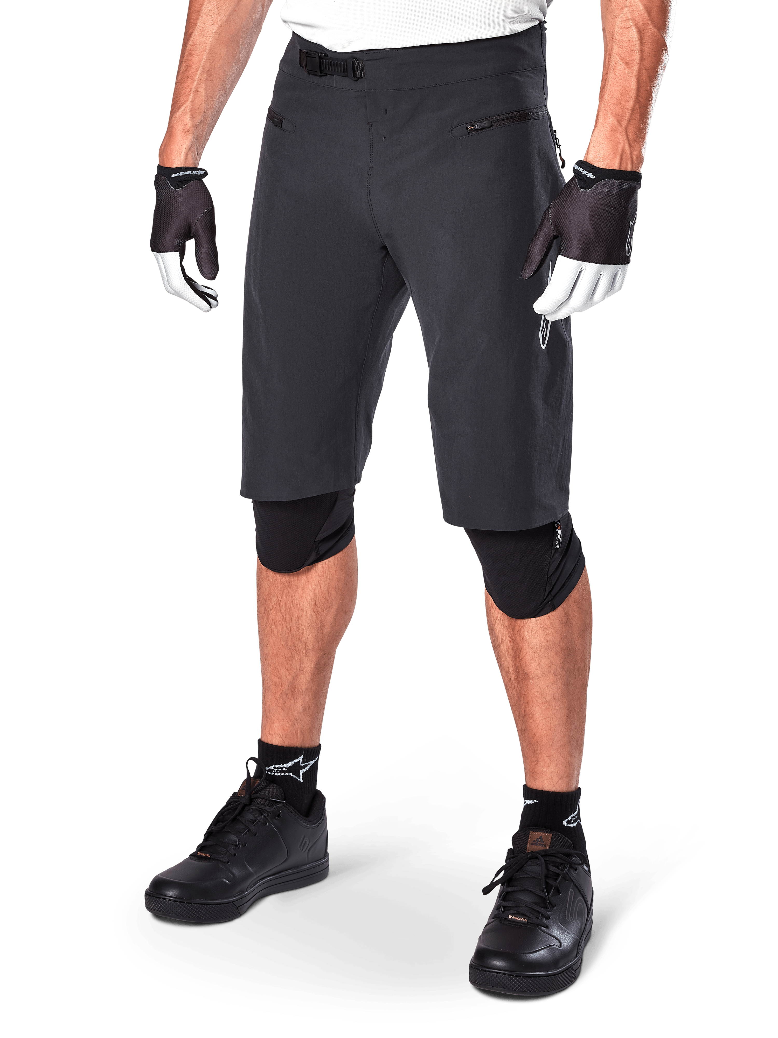Alpinestars A-Aria Shorts, calções de BTT, pretos, pelo joelho com bolsos frontais com fecho e fivela de catraca ajustável na cintura, usados com joelheiras pretas, meias e luvas de ciclismo