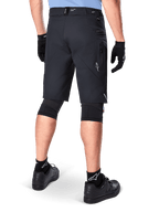 Calções Alpinestars A-Dura Elite, pretos, vista traseira de um ciclista com equipamento de mountain bike, incluindo joelheiras pretas, luvas e meias com logótipos brancos, com bolsos laterais com fecho e detalhes refletores em tecido Cordura resistente.
