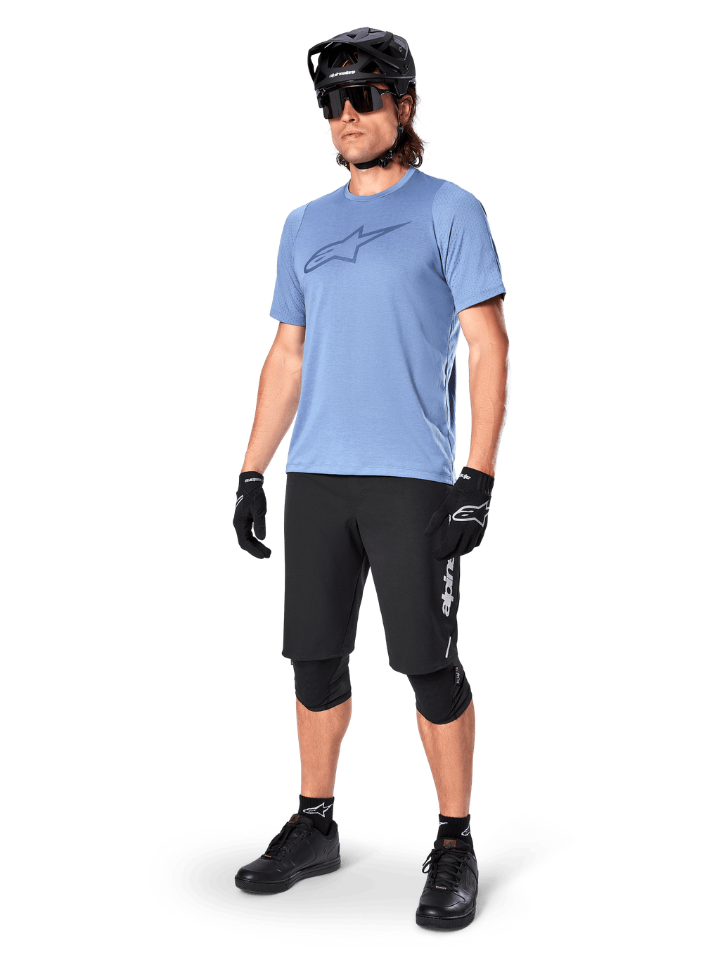 Ciclista masculino com calções Alpinestars A-Dura Elite em preto, camisola de manga curta azul claro com logótipo no peito, capacete preto, óculos de sol e joelheiras de proteção, equipamento completo de mountain bike para trilhos fora de estrada