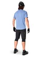 Calções Alpinestars A-Dura Elite, calções de BTT, pretos, vista traseira no modelo, usados com camisola de manga curta azul-claro e equipamento de proteção preto, design técnico com bolsos com fecho e detalhes refletores para ciclismo fora de estrada