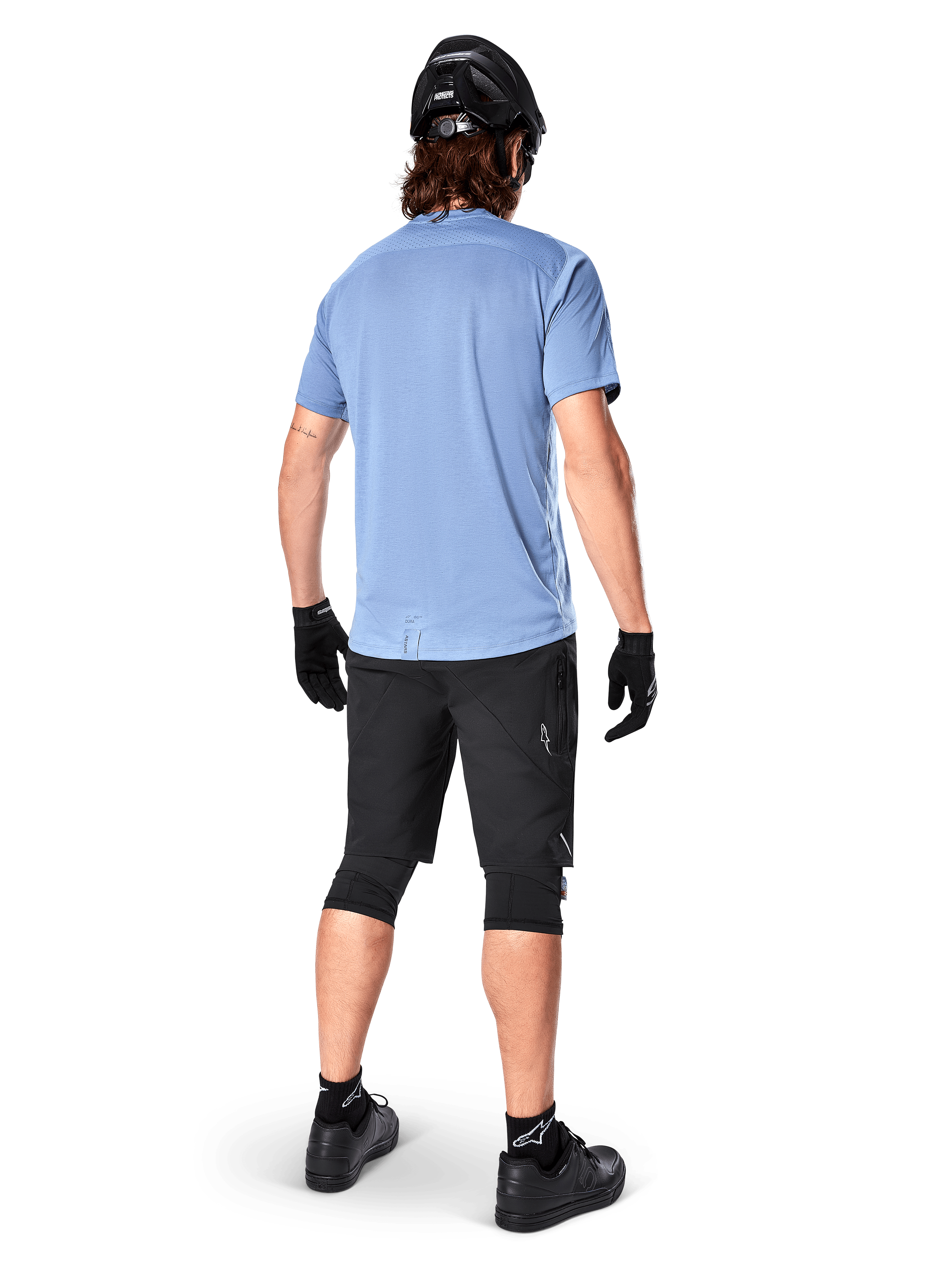 Calções Alpinestars A-Dura Elite, calções de BTT, pretos, vista traseira no modelo, usados com camisola de manga curta azul-claro e equipamento de proteção preto, design técnico com bolsos com fecho e detalhes refletores para ciclismo fora de estrada