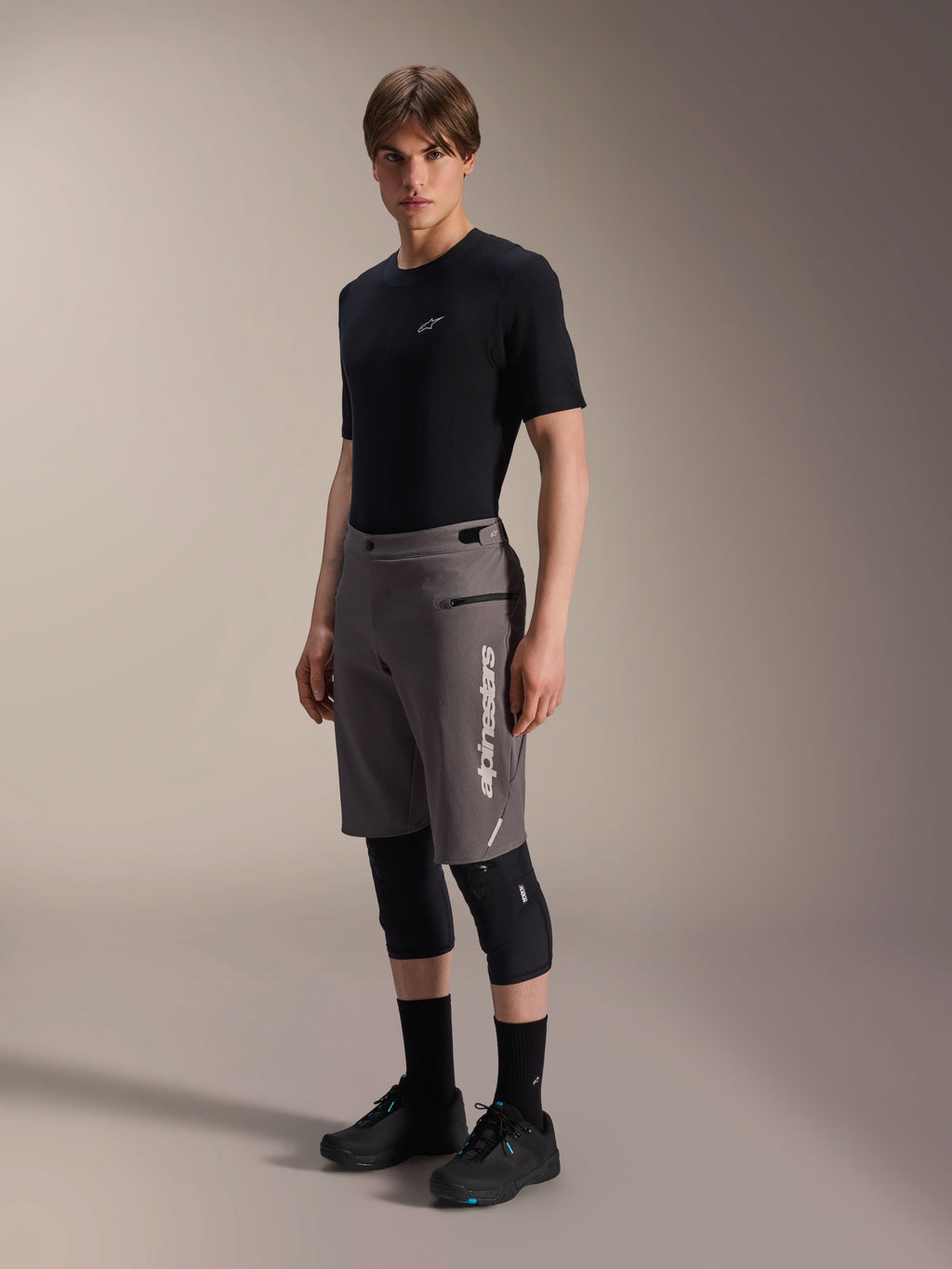 Calções Alpinestars A-Dura Elite, calções de BTT em cinzento escuro, usados por um modelo com t-shirt preta e joelheiras, com um logótipo Alpinestars vertical branco na perna esquerda, tecido técnico Cordura para ciclismo fora de estrada