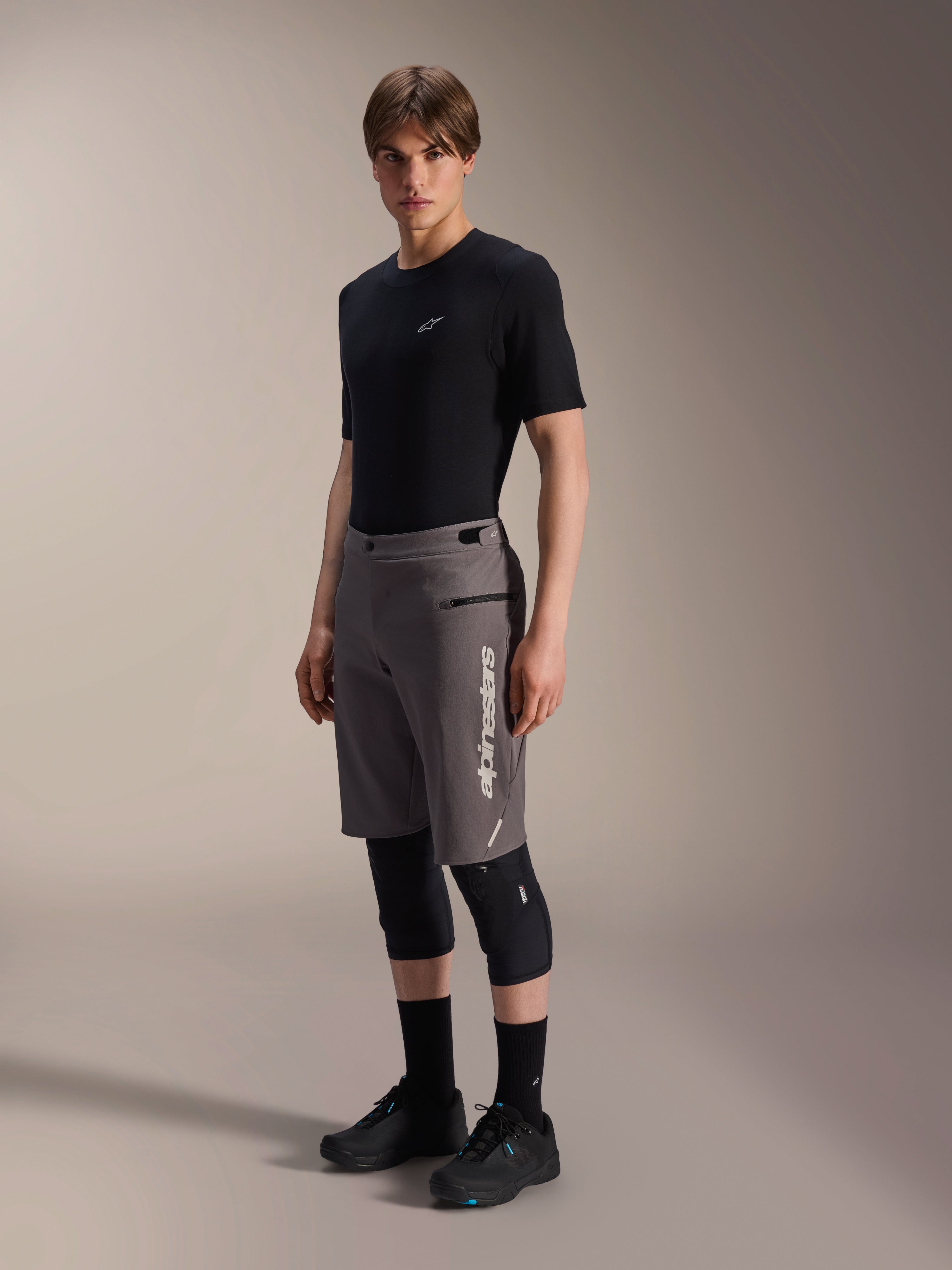 Calções Alpinestars A-Dura Elite, calções de BTT em cinzento escuro, usados por um modelo com t-shirt preta e joelheiras, com um logótipo Alpinestars vertical branco na perna esquerda, tecido técnico Cordura para ciclismo fora de estrada