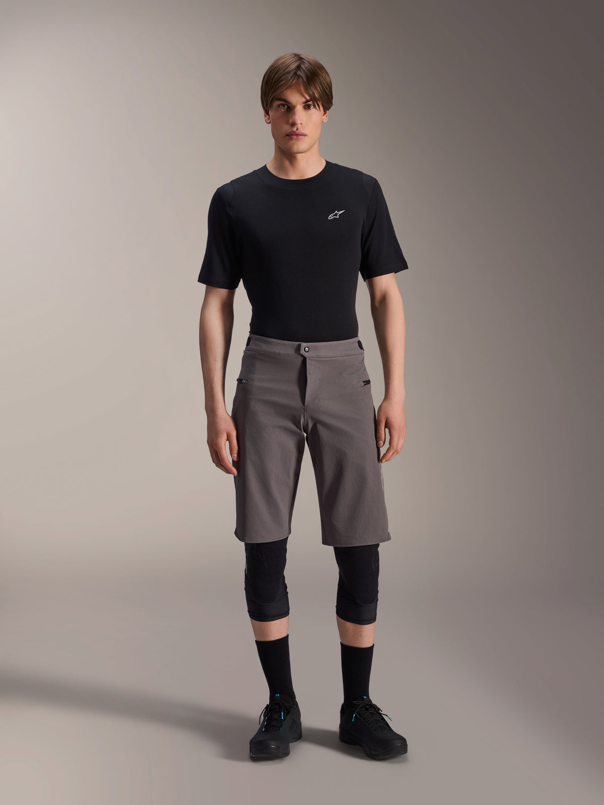 Alpinestars A-Dura Elite Shorts, Dark Gray Mountain Bike Shorts, worn with a black crew neck t-shirt and black knee guards, knee-length performance cycling apparel featuring a front snap closure and durable Cordura fabric.