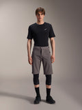 Alpinestars A-Dura Elite Shorts, calções de BTT cinzento escuro, usados com t-shirt preta de gola redonda e joelheiras pretas, vestuário de ciclismo de performance pelo joelho com fecho frontal de mola e tecido Cordura durável
