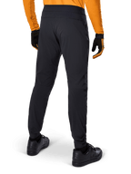 Alpinestars A-Dura Pants, Black MTB Pants, rear view, worn with an orange long-sleeve jersey and black gloves, featuring elasticated cuffs and durable textile material for mountain biking.