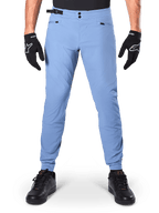 Calças Alpinestars A-Dura, calças de MTB, Infinity Blue, calças de mountain bike em azul claro com fecho de pressão duplo e bolsos com zíper, usadas com luvas pretas e sapatos pretos, ajuste regular com punhos elásticos