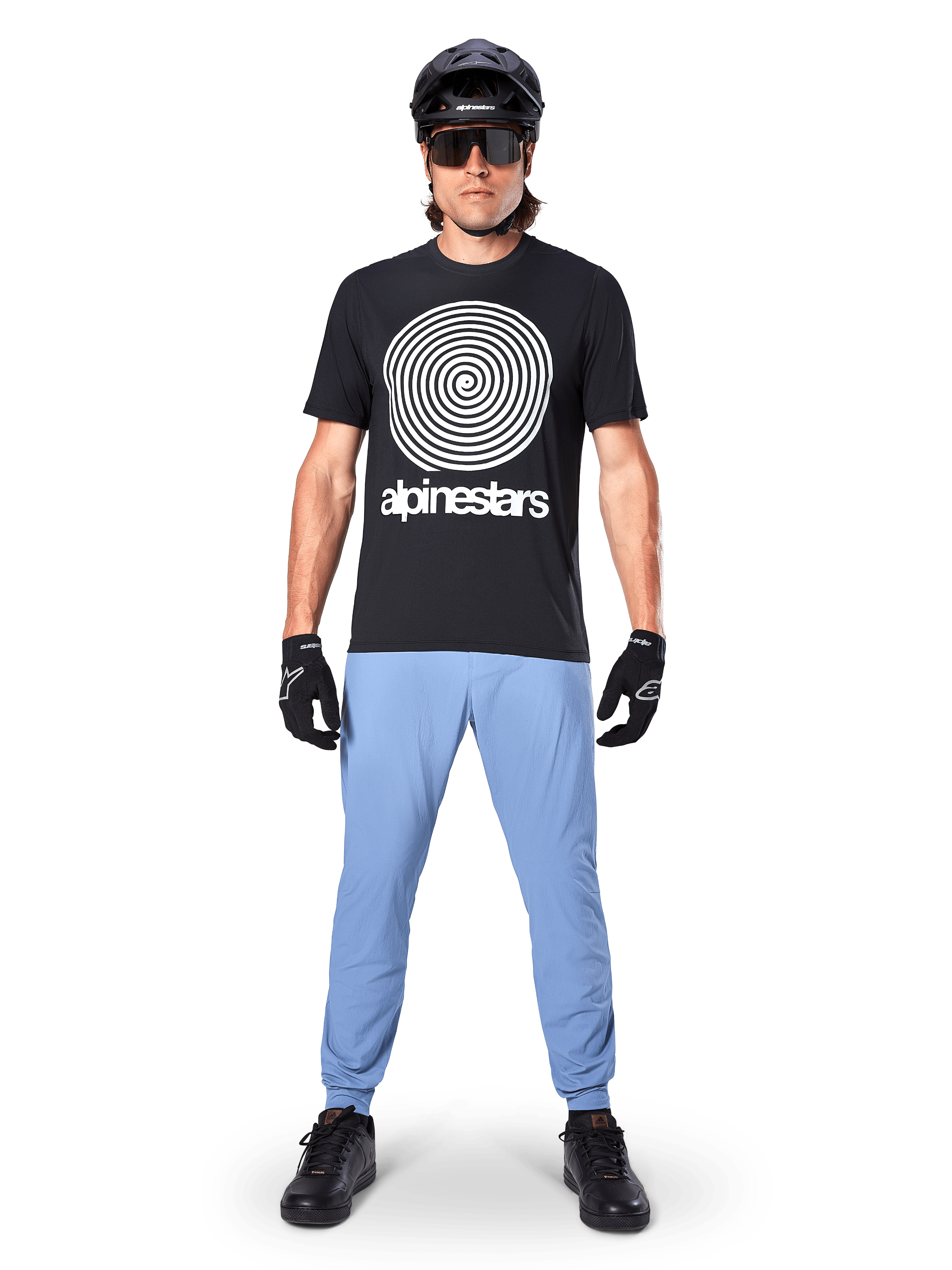 Calças Alpinestars A-Dura, Infinity Blue, calças de MTB usadas com uma t-shirt preta com grafismo em espiral, luvas pretas e capacete preto, com tecido elástico durável e punhos elásticos, equipamento de mountain bike de alta performance